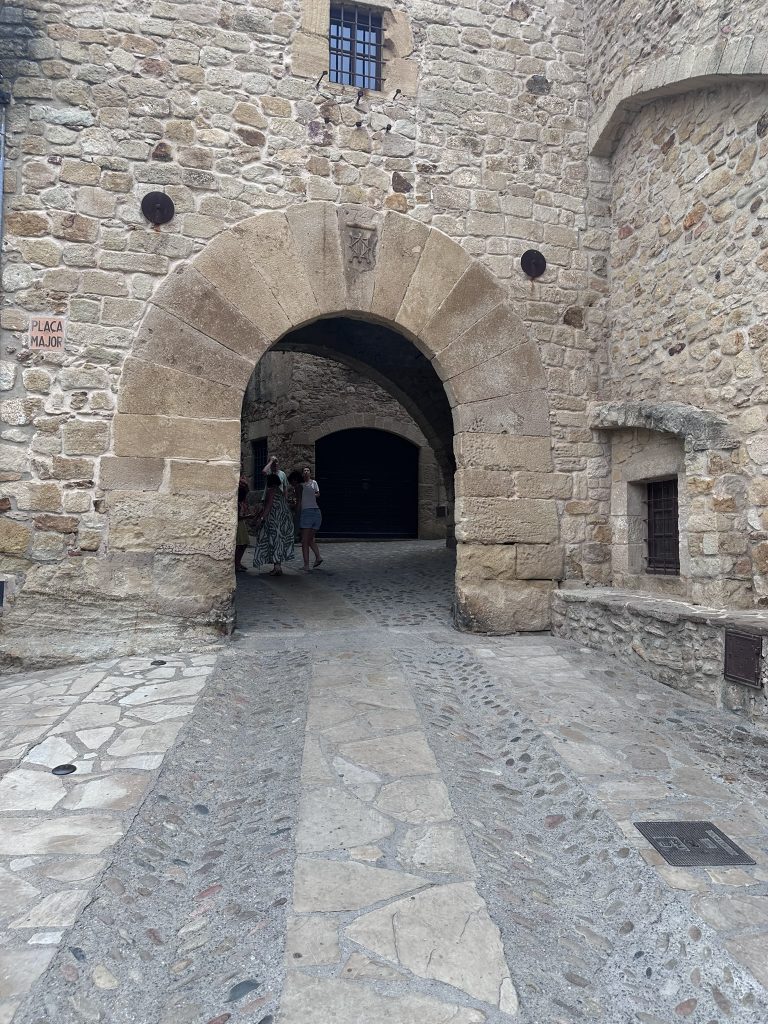 Arco empedrado en una calle estrecha del casco antiguo de Pals, con casas de piedra dorada y detalles florales en los balcones.