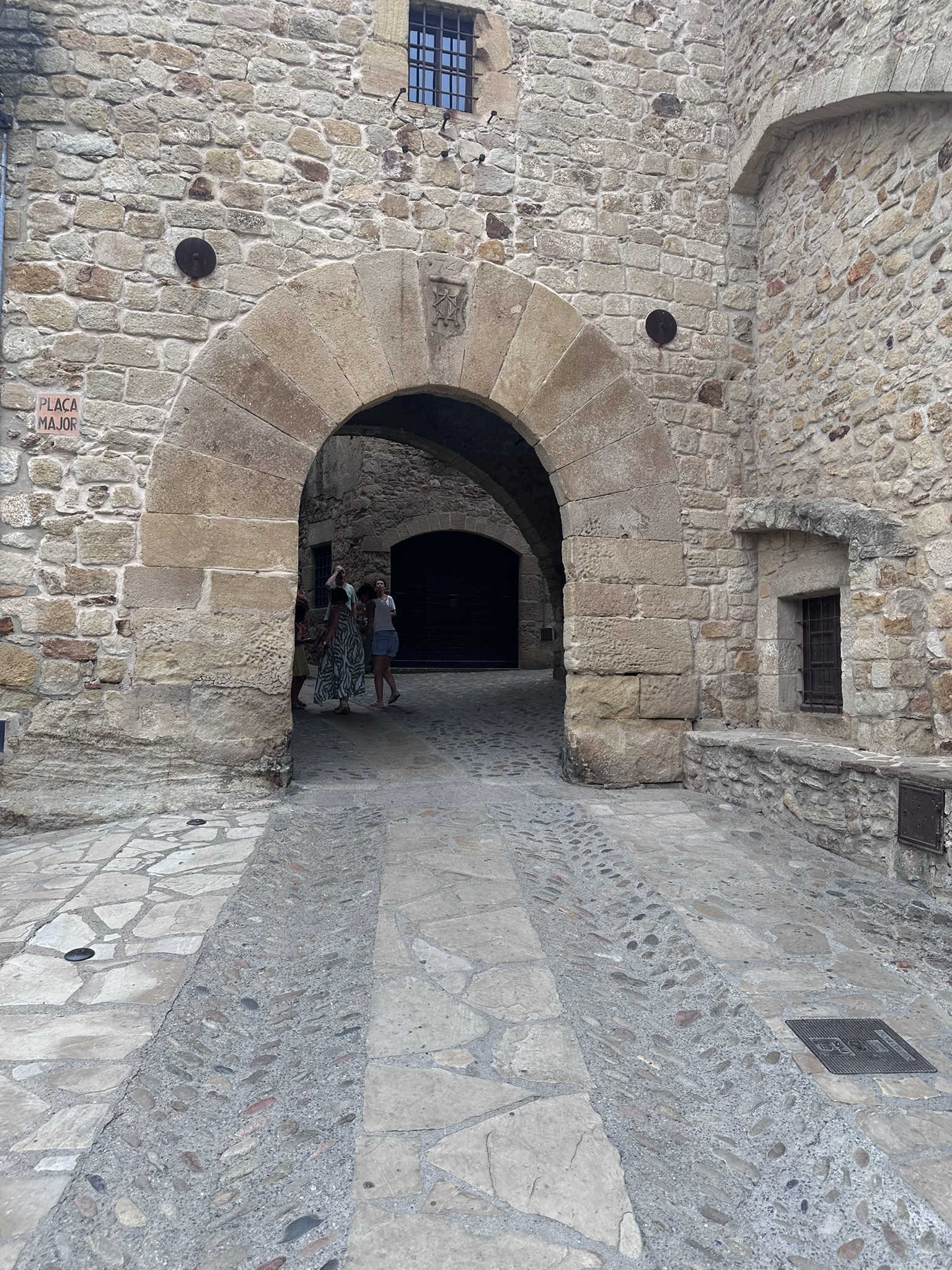Arco empedrado en una calle estrecha del casco antiguo de Pals, con casas de piedra dorada y detalles florales en los balcones.
