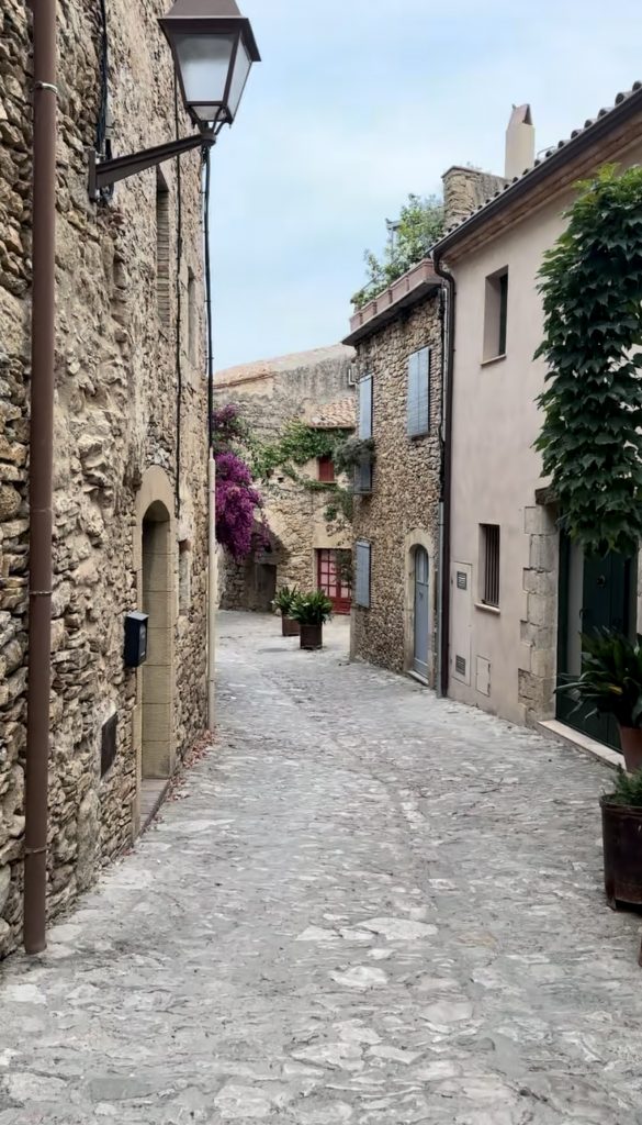 Otra vista de una calle empedrada en Peratallada, rodeada de casas de piedra y vegetación, que conserva el estilo medieval del pueblo.