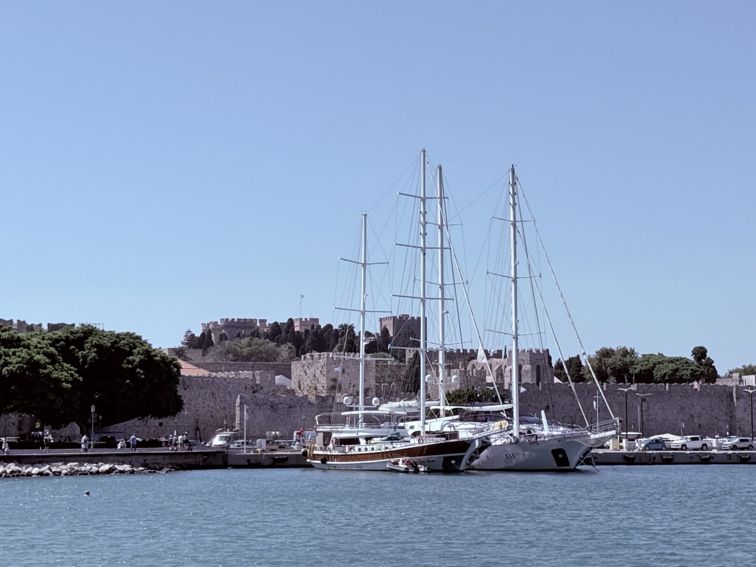 Vista del puerto de Rodas con barcos atracados en el mar y las murallas medievales al fondo