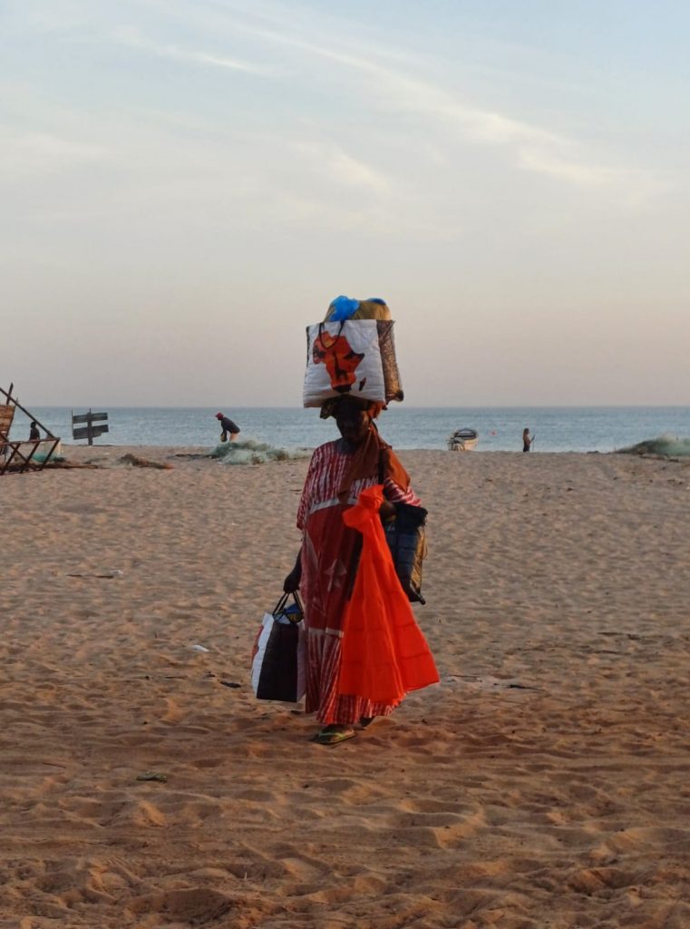 Mujer africana cargando bolsas en la cabeza y en las manos en Saly, Senegal