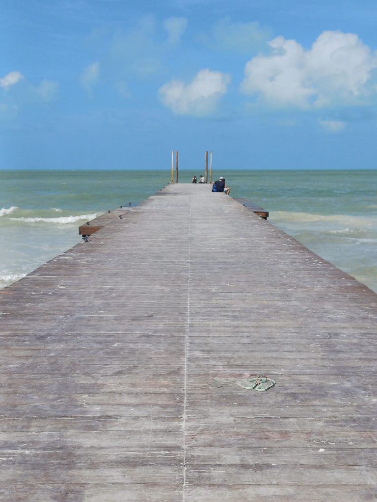 Embarcadero de madera en Holbox con vista al mar Caribe y barcas amarradas sobre el agua turquesa